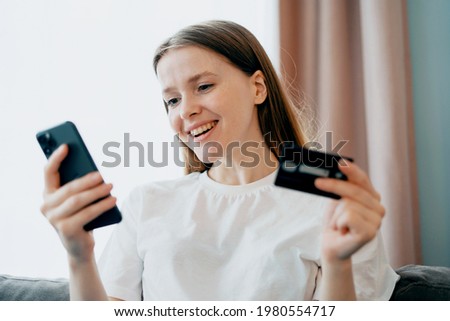 Young female freelance student working at home on the phone. Makes an order online in the apartment in the kitchen. Surfs the Internet looking for purchases on the site.