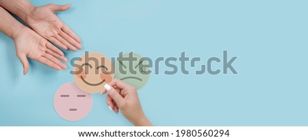 Hand holding paper cut happy smile face on blue background, positive thinking, mental health assessment , world mental health day concept Royalty-Free Stock Photo #1980560294