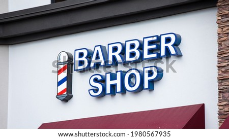 Exterior of a barber shop with a generic sign at its storefront. Classic red, blue, and white icon. Captured during the day in the Las Vegas suburbs of Henderson, NV.