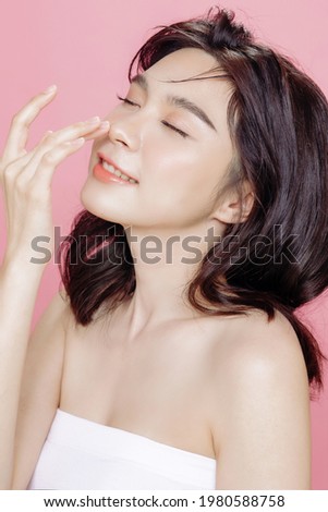 Asian woman has a lovely face is feeling happy with her perfect skin touch her face. She wears a white strapless bra. isolated over pink background. Skincare, cosmetology and plastic surgery concept.