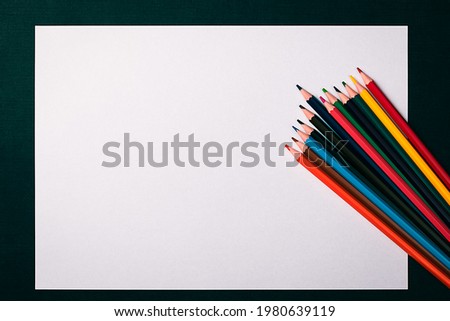 A blank white sheet and colored pencils for drawing on a plain textured background with space for copying and lettering. Layout, mockup free space.