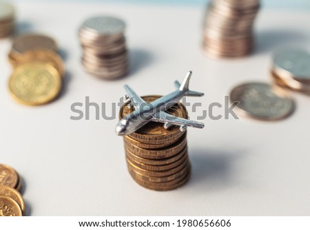The airplane stands on a stack of coins. A toy little airplane is lying sideways on the gold coins. Royalty-Free Stock Photo #1980656606