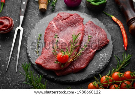 Meat. Raw veal steak with rosemary and spices. On a black stone background. Top view. Royalty-Free Stock Photo #1980660122