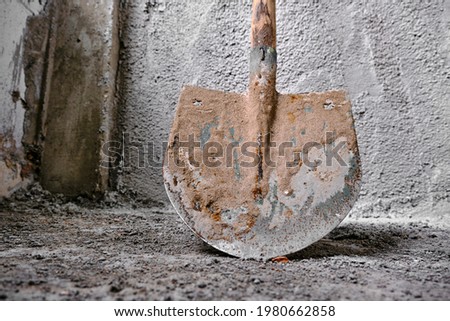 Construction works of plastering. photo taken low angle shovel in front of the recently made plastered wall by concrete. Green colors exist on metal side of shovel.