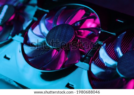 Gaming graphics card with neon magenta-cyan illumination and high-speed fans. Video chip for mining and powerful games in the cyberpunk concept. Selective Focus