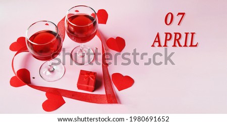 calendar date on light background with two glasses of red wine, red gift box and red hearts with copy space.  April 7 is the seventh day of the month.