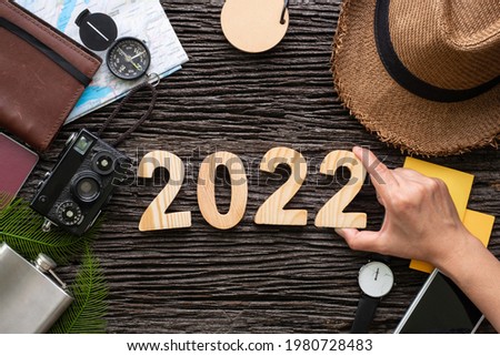 top view hand putting 2022 happy new year number on wood table with adventure accessory item,holiday vacation planning.