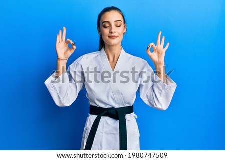 Beautiful brunette young woman wearing karate fighter uniform with black belt relax and smiling with eyes closed doing meditation gesture with fingers. yoga concept. 