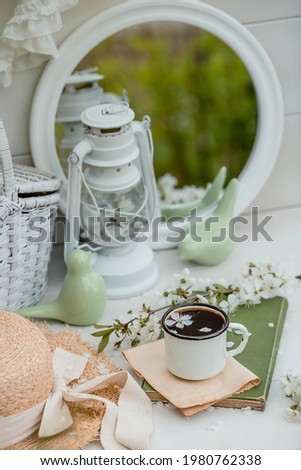 Visual for content. Still life in vintage style. A mug of coffee, an old book, a straw hat, a mirror, and a cherry blossom in the garden on a wooden table.
