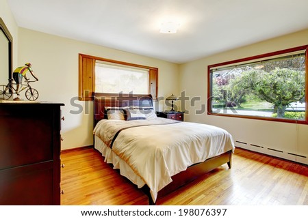 Ivory bedroom with dark brown wooden furniture set, shiny new hardwood floor and wide window