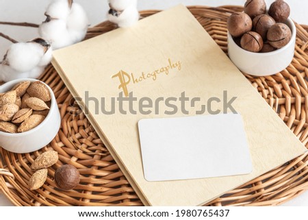 Stylish composition of blank business card photobook and delicious nuts lying on wicker tray on table extreme close view