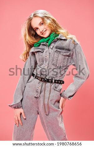 Youth style. Pretty teenage girl in denim overalls and with wavy blonde hair smiling at camera.   