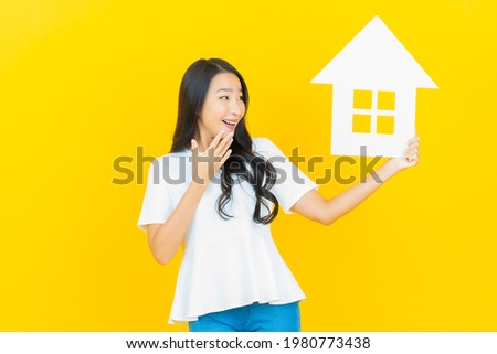 Portrait beautiful young asian woman with house or home paper sign on yellow color background