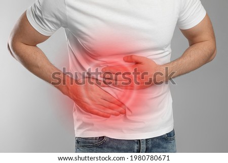 Man suffering from pain in lower right abdomen on light grey background, closeup. Acute appendicitis Royalty-Free Stock Photo #1980780671