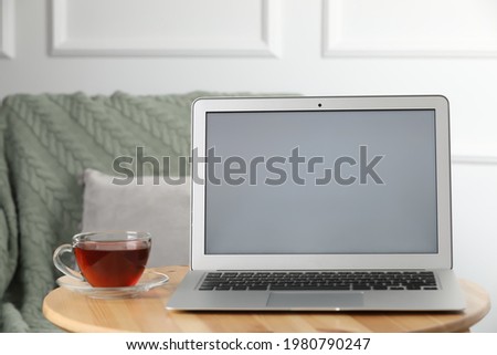 Modern laptop and cup of tea on wooden table indoors