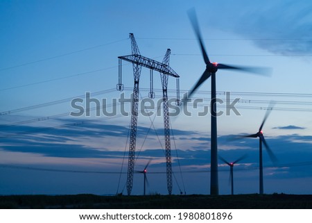 Wind turbines and electricity poles during a summer evening, renewable green energy. Power station in a wind mill farm. Copy space. Royalty-Free Stock Photo #1980801896