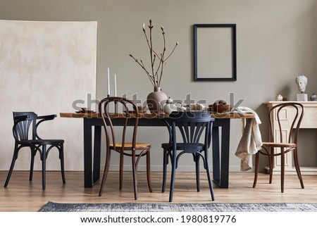Stylish rustic interior of dining room with walnut wooden table, retro chairs, decoration, fireplace, dried flower, candlestick mock up picture frame and carpet in minimalist home decor. Template. Royalty-Free Stock Photo #1980819776