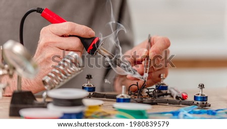Closeup view of man hands during quadcopter repairing process using soldering iron for wires Royalty-Free Stock Photo #1980839579