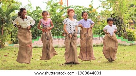 Group of Childrens playing potato sack jumping race at park outdoor during summer camp - kids having fun while playing gunny sack racing competition Royalty-Free Stock Photo #1980844001