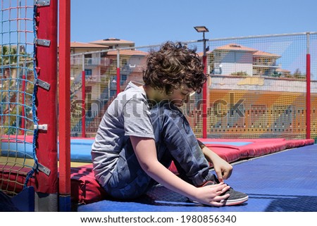 a child is tying his shoes in front of the playground door, near the trampolines
