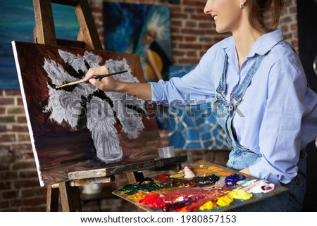 Young beautiful female artist painting still life with sunflower on canvas using oil paintings and art brush. Painter creating artwork in art studio. Relaxation, leisure, hobby, stress management.