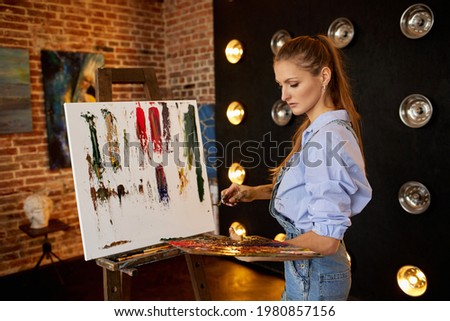 Painter at the studio creating abstract picture on canvas using oil paintings and palette knife. Young female artist working. Creative process, relax,leisure,hobby, stress management