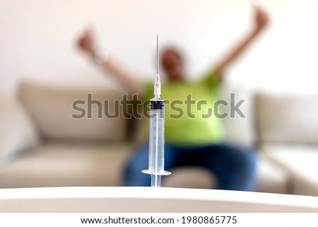 Photo of a syringe with a senior man blurred out in the background. Senior man looking at vaccine isolated on the white background. Happy elderly man is about to received dose of vaccine for COVID-19.