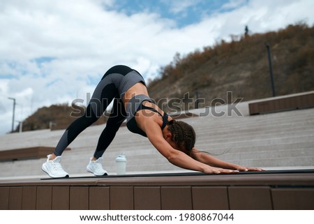 Beautiful smiling sportswoman stretches her leg during training. morning stretching on the rug in the park. concrete floor