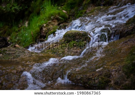 sandy rock along which flows a clear forest spring water forming a waterfall. Stones with green moss. Royalty-Free Stock Photo #1980867365