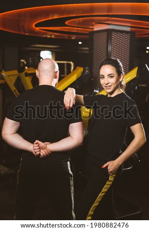 A group of people: an athletic woman and a muscular man. Team of trainers in the same clothes posing for the camera against the background of the gym