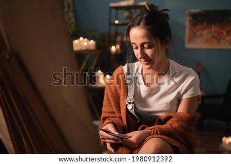 A woman of young age sits in her homespun clothes in the living room and looks through the new drawing pencils she bought, wondering which one to use to paint portrait