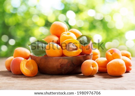 Bowl of fresh apricots on a wooden table over blurred green background Royalty-Free Stock Photo #1980976706