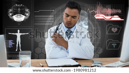 Composition of male doctor sitting at desk reading, with medical research data interface screen. global medicine, research and digital interface concept digitally generated image.