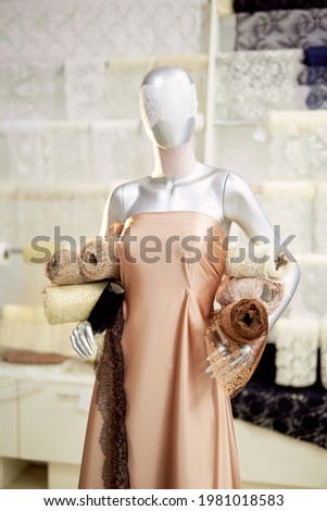 Fashion, bespoke, tailoring or needlework concept. Mannequin or dummy with beige and brown cloth and linen textile rolls in hands at studio, atelier or drapery store. High quality vertical image