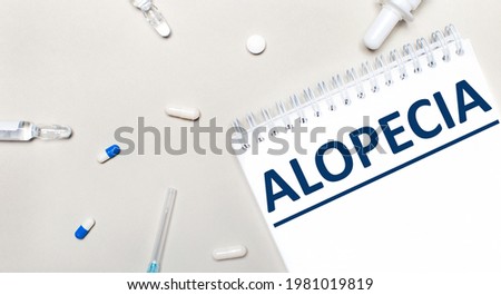 On a light background, a syringe, a stethoscope, vials of medicine, an ampoule and a white notepad with the text ALOPECIA. Medical concept