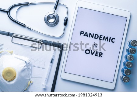 End of pandemic. Syringe with needle, hospital healthcare charts, doctor stethoscope and white tablet with text on screen for medical equipment background. Pandemic is over concept