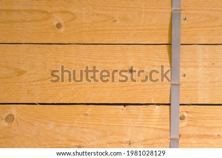 A flat wall of three yellow, pine planks joined together. The boards are not processed, rough. The boards are arranged horizontally, held together with iron nails and steel tape nailed down with clips