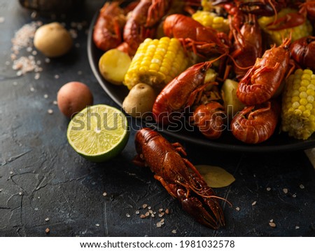 Pictured is a black dining table with boiled crayfish and boiled corn in a large black plate. There are also lemon, crayfish and potatoes on the table. Bright colors of ingredients