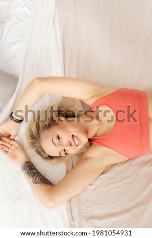 Young blonde-hair girl waking up, smiling, looking at the camera. Beautiful woman in a good mood lies on the bed, stretching out, getting ready for morning training
