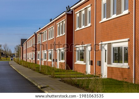 Brand new development of basic public housing in a village in the Netherlands. Neighborhood scene of street with modern suburban terraced houses. Royalty-Free Stock Photo #1981063535