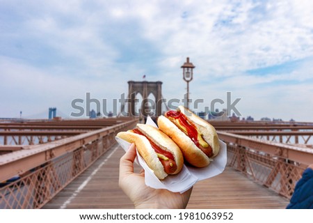 Holding two hot dogs in NYC on the Brooklyn Bridge . Royalty-Free Stock Photo #1981063952