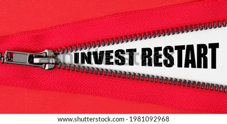 Finance and business concept. Against the background of red fabric, a zipper opens, on the white surface the inscription - INVEST RESTART