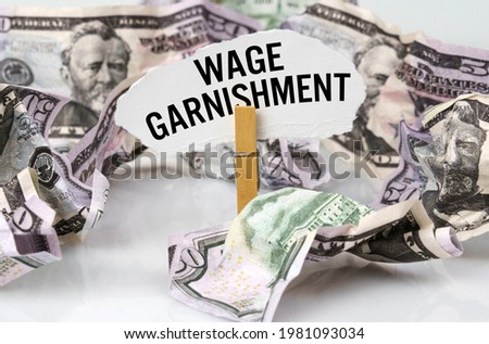 Business and finance concept. There are dollars on the table and there is a clothespin with paper on which it is written - WAGE GARNISHMENT Royalty-Free Stock Photo #1981093034