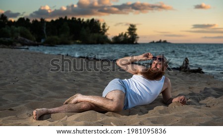 Funny bald man with red beard dressed in underwear posing on the beach. A humorous male parody of a glamorous girl.