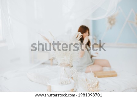 Blurred photo of Young woman plus size model in a green pajama suit drinking coffee in the bed early morning in a modern light interior in light bedroom with canopy