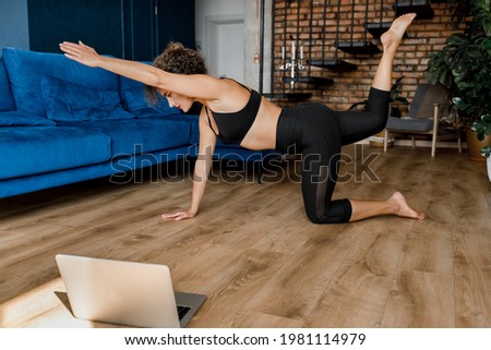 Healthy millennial Caucasian woman watch online sports yoga lesson on laptop doing morning gymnastics in living room at home. Active young female practice yoga or stretching on webcam on computer.