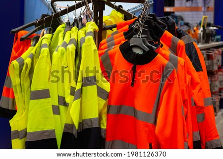 Photo of various colored worker signal jackets hanging on rack on construction supply store shelf.