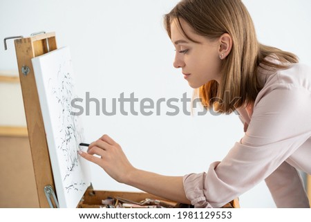 Visual art. Drawing hobby. Creative skill. Painting class. Inspired left-handed female artist sketching picture with pencil on canvas in light studio.