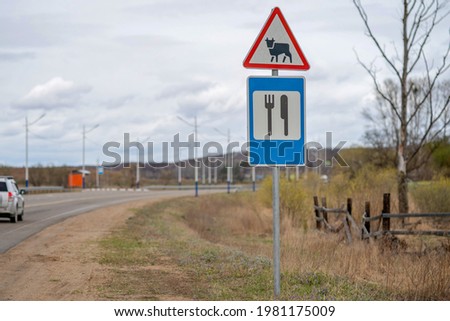 Road signs near the highway in the countryside. A funny combination of two road signs of a cattle drive and a food point