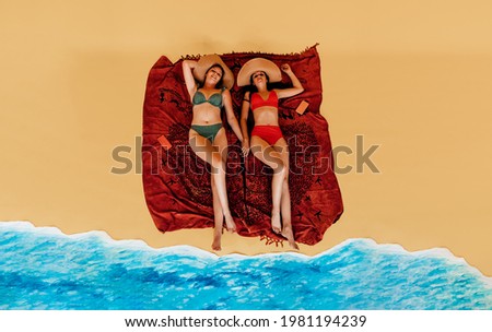 top view of two young bikini girls with straw hats lying down and relaxing at the beach. studio shot, vacation concept.